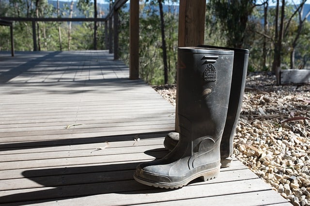 A pair of black rubber wellies stands on a wooden decking, partly in sunlight, with pebbles and trees visible in the background—echoing moments from Coping With My Child's First School Residential.