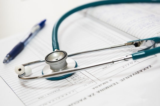 A teal stethoscope rests on a medical form with printed text, next to a blue pen and an open notebook, highlighting a UK healthcare setting and hinting at the role of documentation in avoiding misconceptions or medical negligence claims.