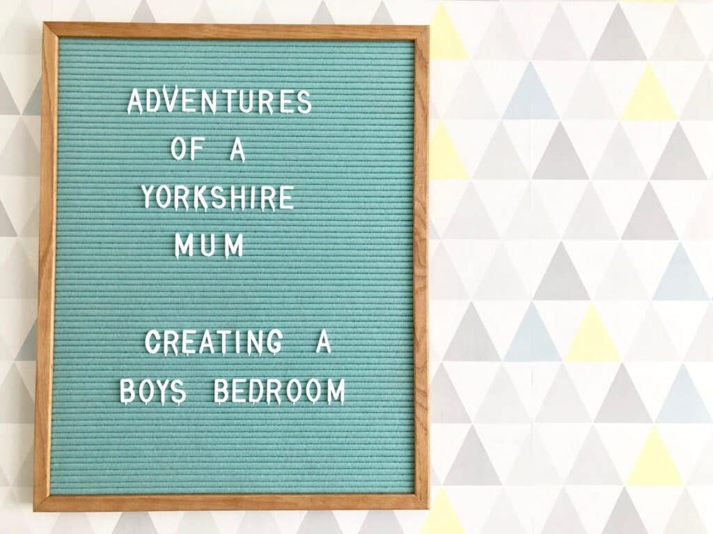 A felt letter board framed in wood displays the words: "Adventures of a Yorkshire Mum Creating a Boys' Bedroom" against geometric pastel wallpaper—a charming touch for boys' bedroom or children's room decor inspiration.