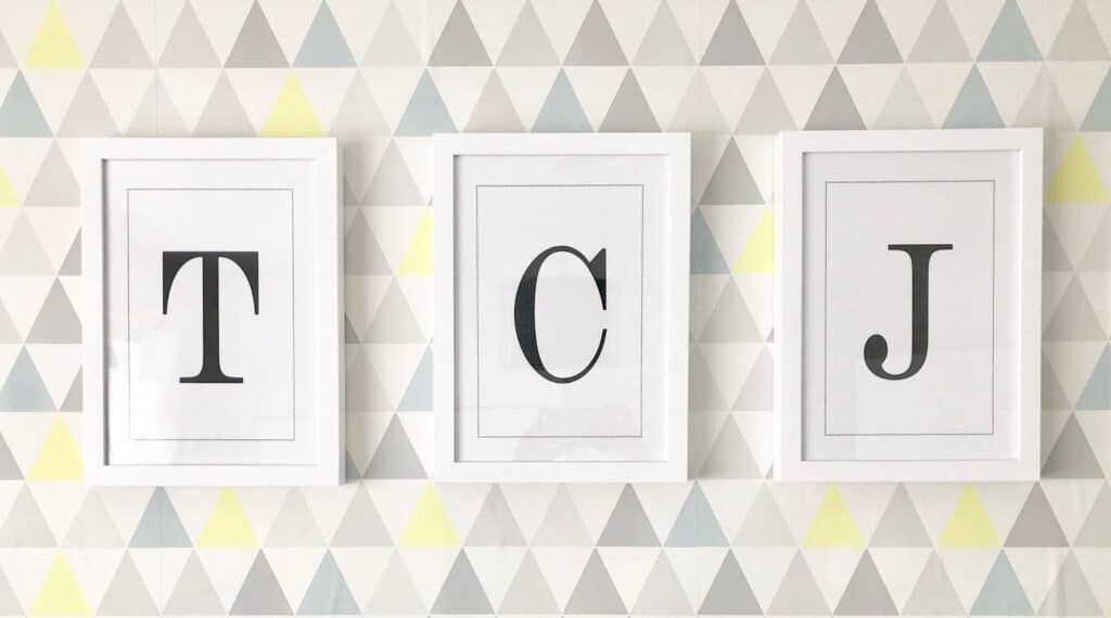 Three white-framed pictures hang on a wall with a geometric triangle pattern—stylish bedroom decor that's perfect for boys' bedrooms or anyone seeking unique boys' room ideas. Each frame displays a large black letter: "T", "C", and "J".