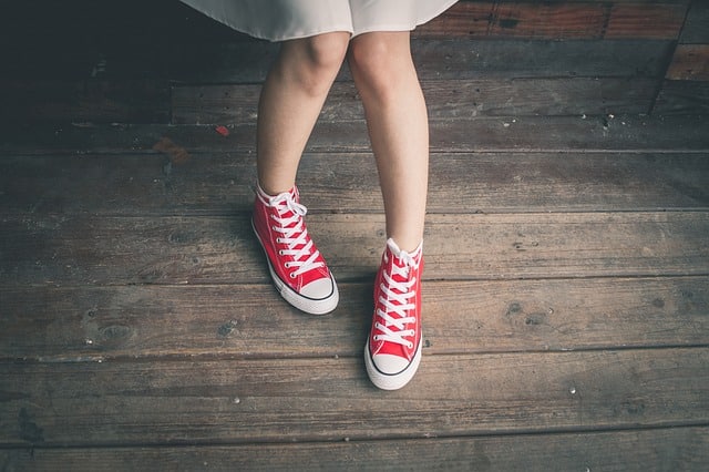 Person wearing a white skirt and red high-top trainers standing on a wooden floor, showcasing the growing influence of gender-neutral clothing in the fashion industry. Only their legs and feet are visible in the image.