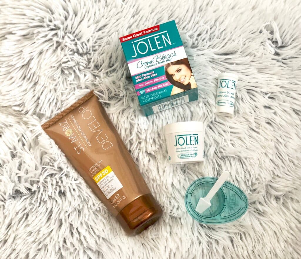 A tube of St. Moriz self-tanning lotion and several Jolen Creme Bleach products are displayed on a fluffy white surface, making them perfect pre-holiday beauty essentials for a radiant, flawless look.