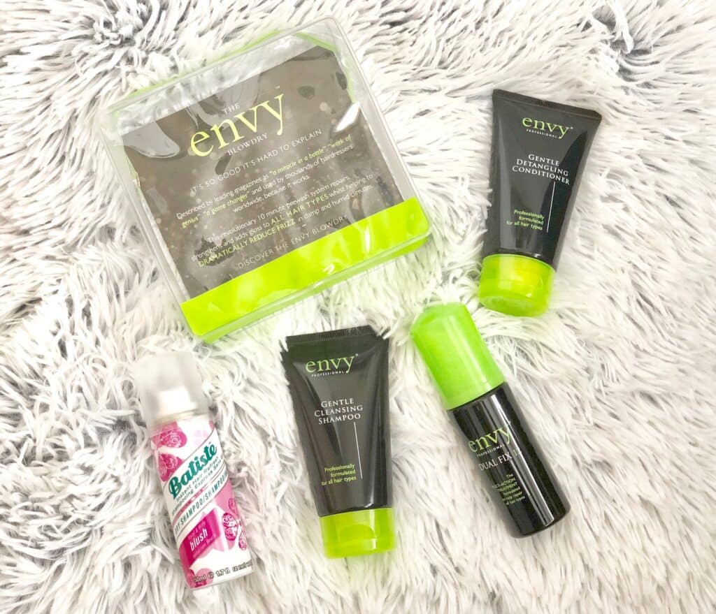 Five hair care products, including four Envy brand items and one Batiste dry shampoo, are arranged on a soft, white faux fur surface—perfect pre-holiday beauty essentials to keep your hair looking its best all season.