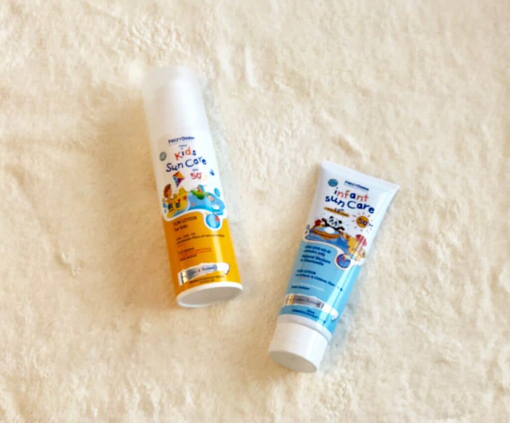 Two tubes of suncream, labelled "Kids Sun Care" and "Infant Sun Care," rest on a soft, light-coloured surface—perfect children's holiday essentials for sun protection. The Kids tube is yellow and white; the Infant one is blue and white.