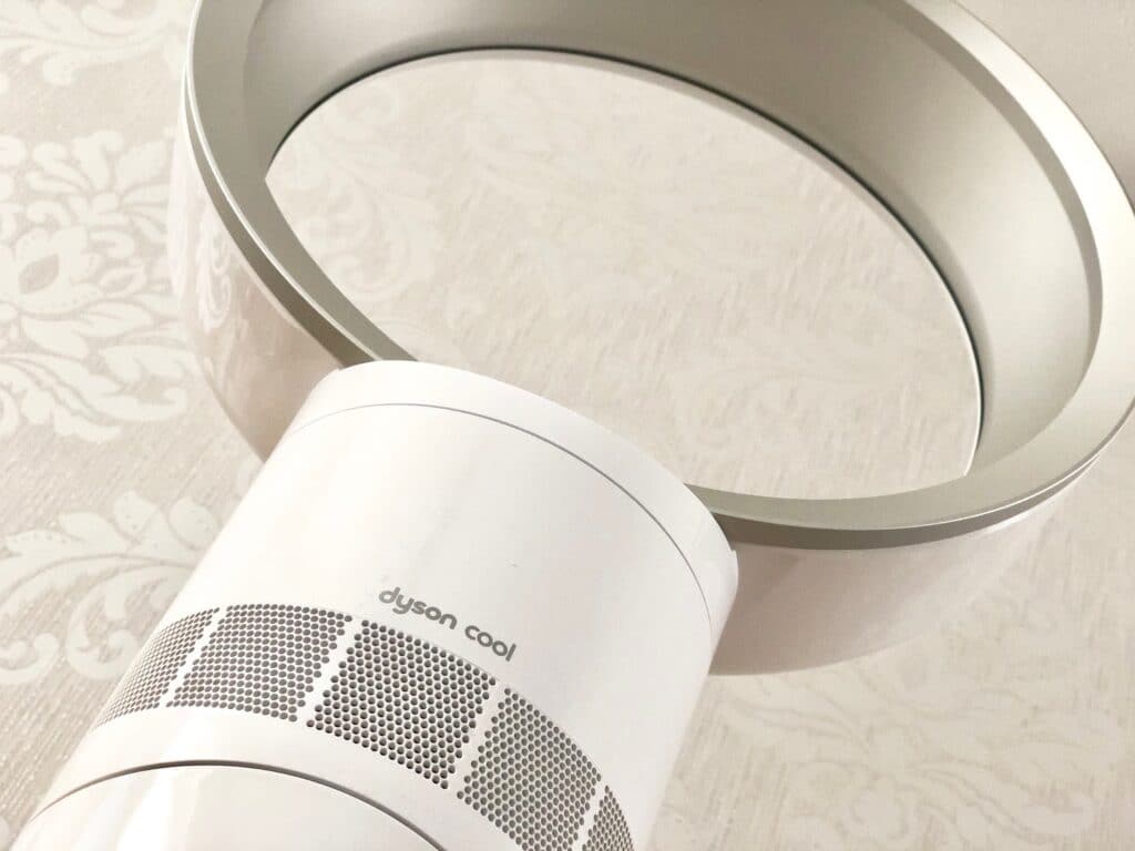 A close-up of the white Dyson AM06 Cool Fan, showing the circular ring and part of the base against a light, patterned background—perfect for those seeking a detailed review of innovative bladeless fans.
