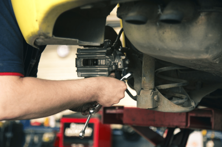A mechanic uses a spanner to work on the suspension or brake system of a car raised on a lift, demonstrating essential family car maintenance in a car repair garage.