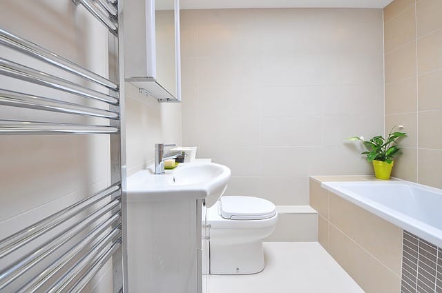 Modern bathroom with beige tiles, a white basin and toilet, a chrome towel rail, built-in bath, and a green potted plant in a yellow pot—this clean, bright space is perfect for home improvement to add value to your home.