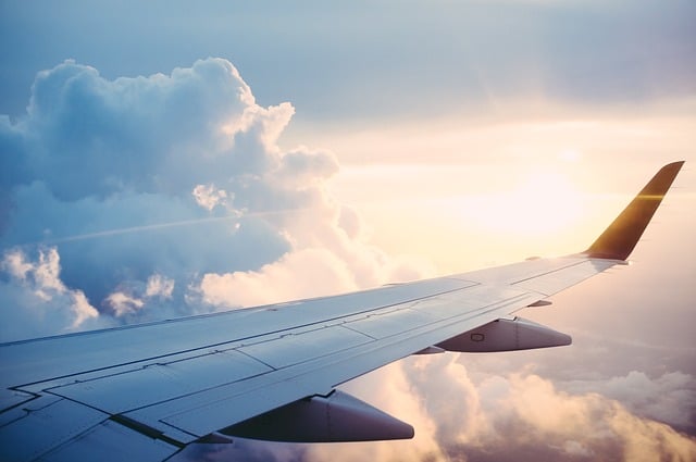 View of an aeroplane wing in flight, with bright sunlight shining through clouds in a blue sky—perfect inspiration for your Summer Holiday Outfit wishlist on Spartoo.