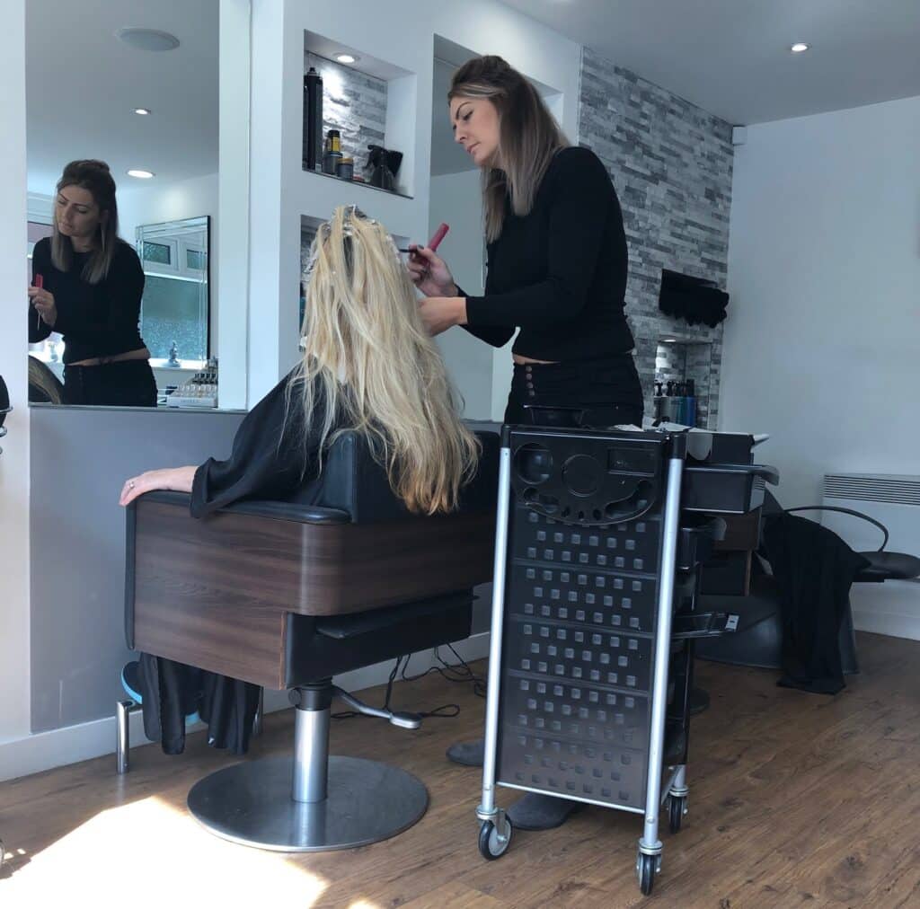 A hairstylist applies colour or highlights to a woman's long blonde hair in a modern, well-lit salon—a perfect setting for a Mum and Daughter Glam Day, with both enjoying premium pampering and style together.