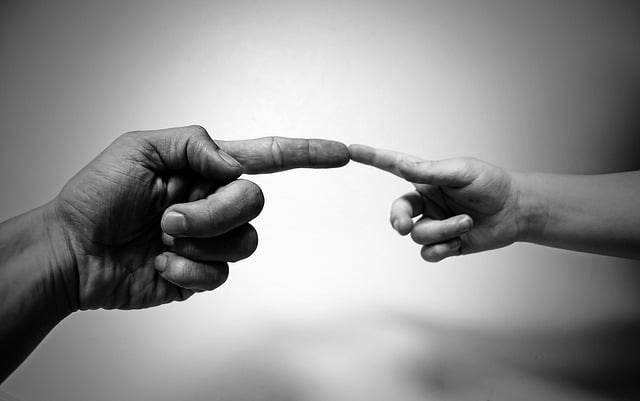 A black-and-white photo showing an adult hand and a child’s hand reaching out to touch each other's index fingers against a blurred background, symbolising the importance of family skills in nurturing strong connections.