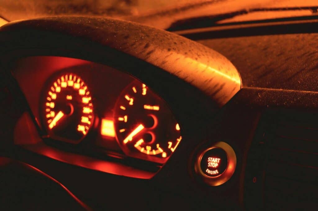 Close-up of a car dashboard at night showing an illuminated speedometer, rev counter, and glowing "Start Stop Engine" button—highlighting the importance of regular car maintenance for smooth driving and money-saving benefits.
