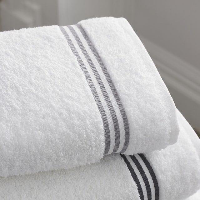 Two neatly folded white towels with grey striped bands near the edge are stacked on top of each other in a bright, clean setting—perfect for those seeking simple bathroom ideas.