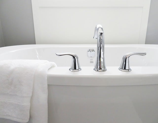 A clean, white bath with modern chrome taps; a folded white towel hangs over the edge. The simple background with light-coloured walls and panelling offers inspiration for choosing a perfect bathroom.