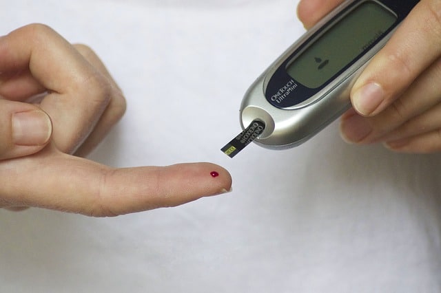 A person uses a blood glucose metre to test their blood sugar by holding a test strip to a drop of blood on their fingertip, an important step in monitoring health conditions and spotting early signs of issues.