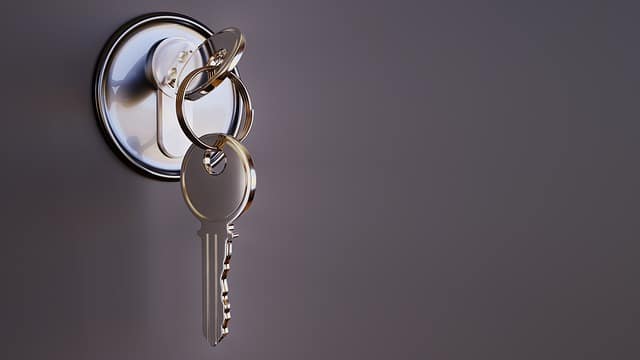 A close-up of a silver key inserted into a door lock, with two additional keys hanging on the keyring. The blurred background highlights this simple solution for effective home protection.