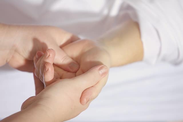 A close-up of one person gently holding and massaging another's hand on a white surface, suggesting care or comfort for someone experiencing health conditions or symptoms.