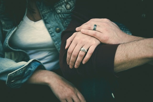 Close-up of a couple sitting together, hands gently resting on each other’s arm, both wearing rings. Their quiet intimacy hints at handling conflict with tenderness, reflecting connection even in moments of marriage conflict resolution.