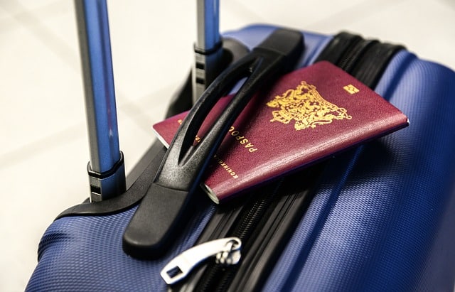 A close-up of a dark blue suitcase with a zip, featuring two silver handles. A maroon passport with a gold emblem rests on top—perfect inspiration for a cruise packing guide or tips for first-time cruisers.