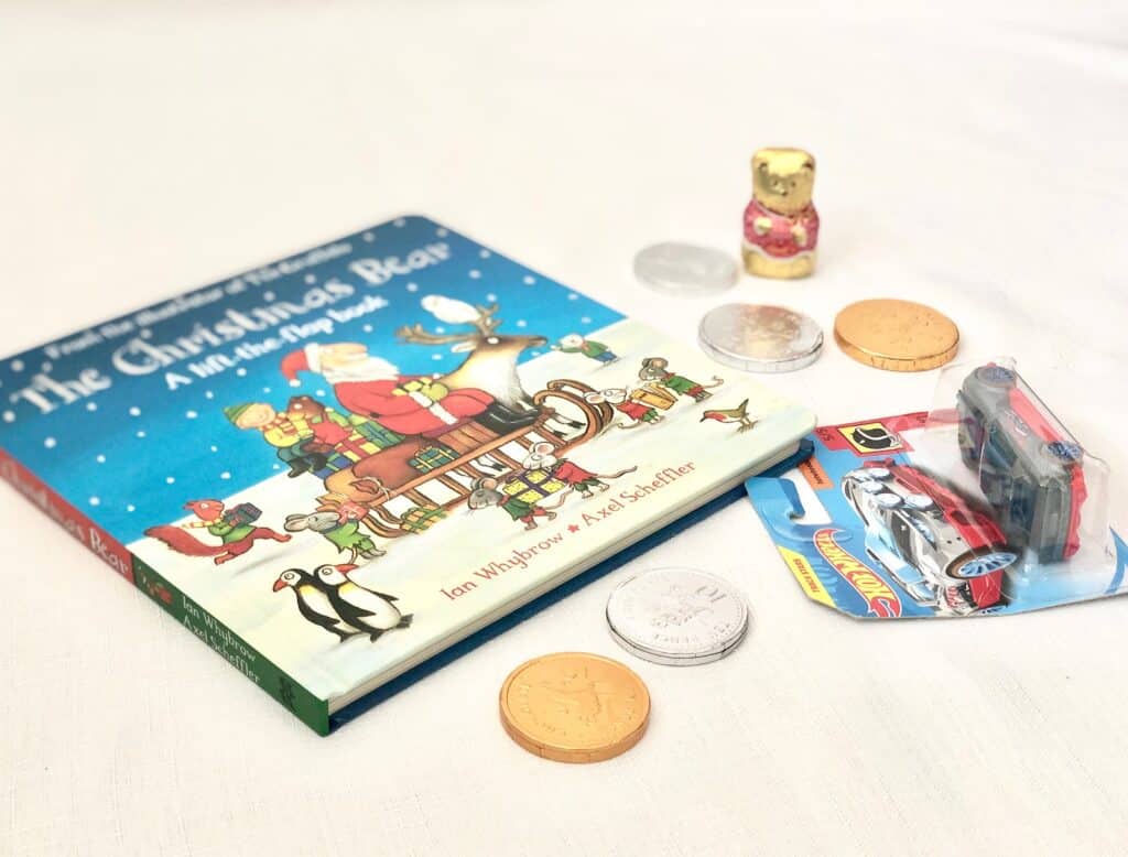 A children’s book titled "The Christmas Bear", toy car in packaging, chocolate coins, and a small chocolate bear are arranged on a white surface—perfect for a magical Christmas Eve Box.
