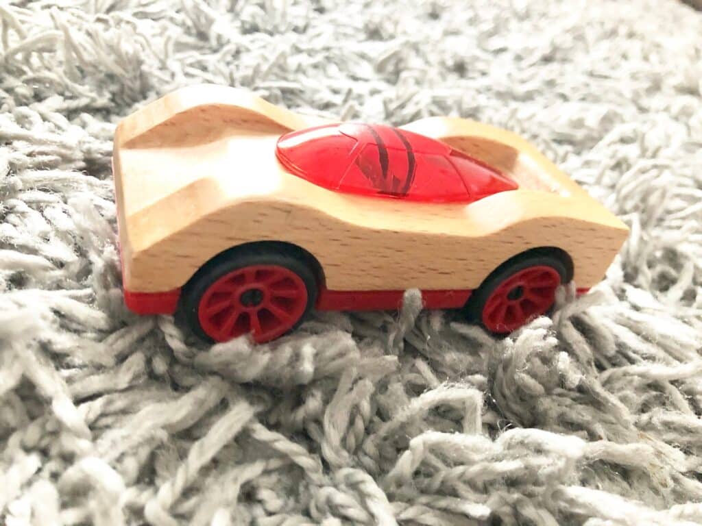 A small wooden toy car with red wheels and a red transparent top sits on a textured, light grey rug—an ideal choice for Christmas presents from Wicked Uncle.