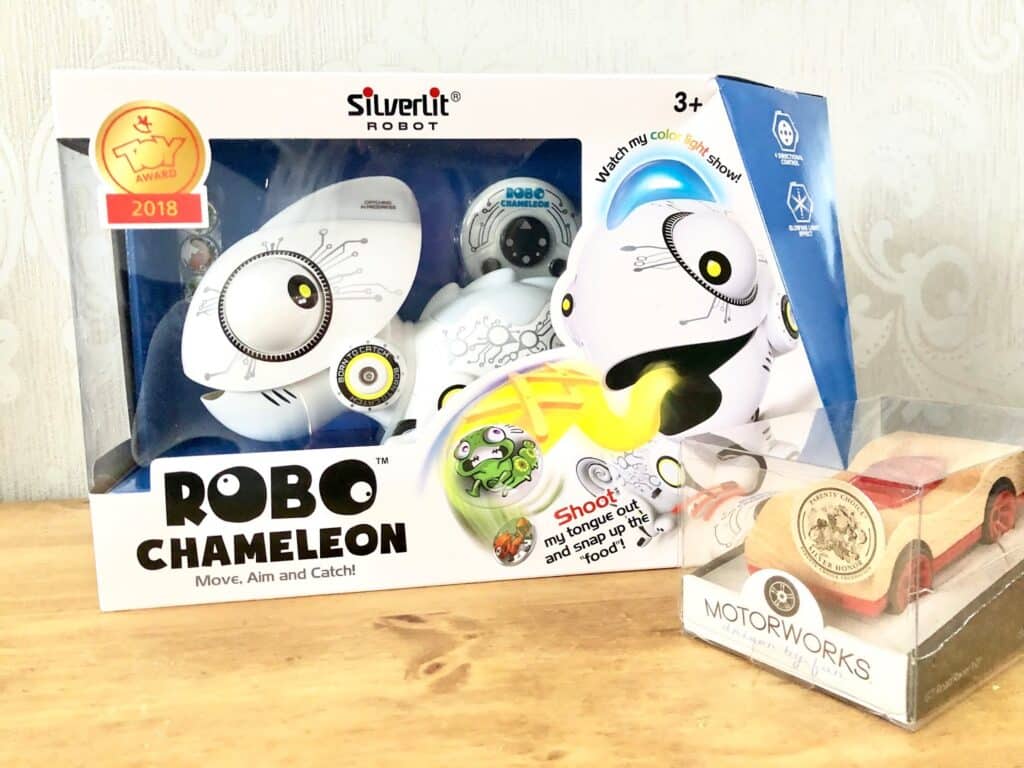 A boxed Robo Chameleon toy with a “2018 Award” badge sits next to a small wooden Motorworks toy car, both on a light wood surface—unique Christmas presents from Wicked Uncle against a pale patterned background.