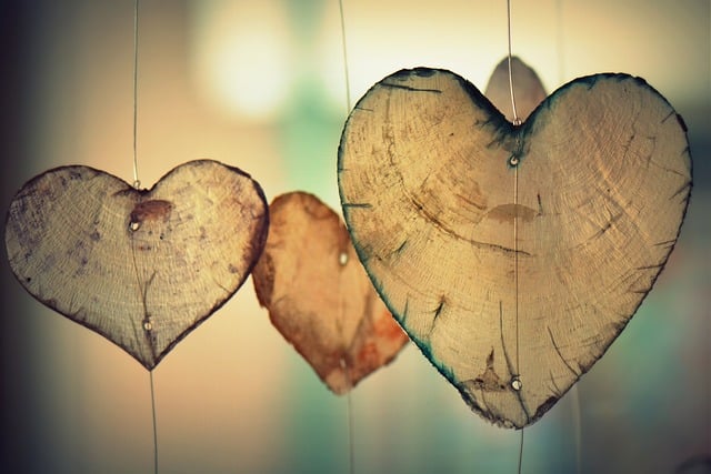 Three wooden heart-shaped ornaments hang by thin strings. The background is softly blurred with warm, gentle lighting, creating a cosy and romantic atmosphere—perfect for inspiring alternative Valentine’s gestures or unique Valentine’s ideas.