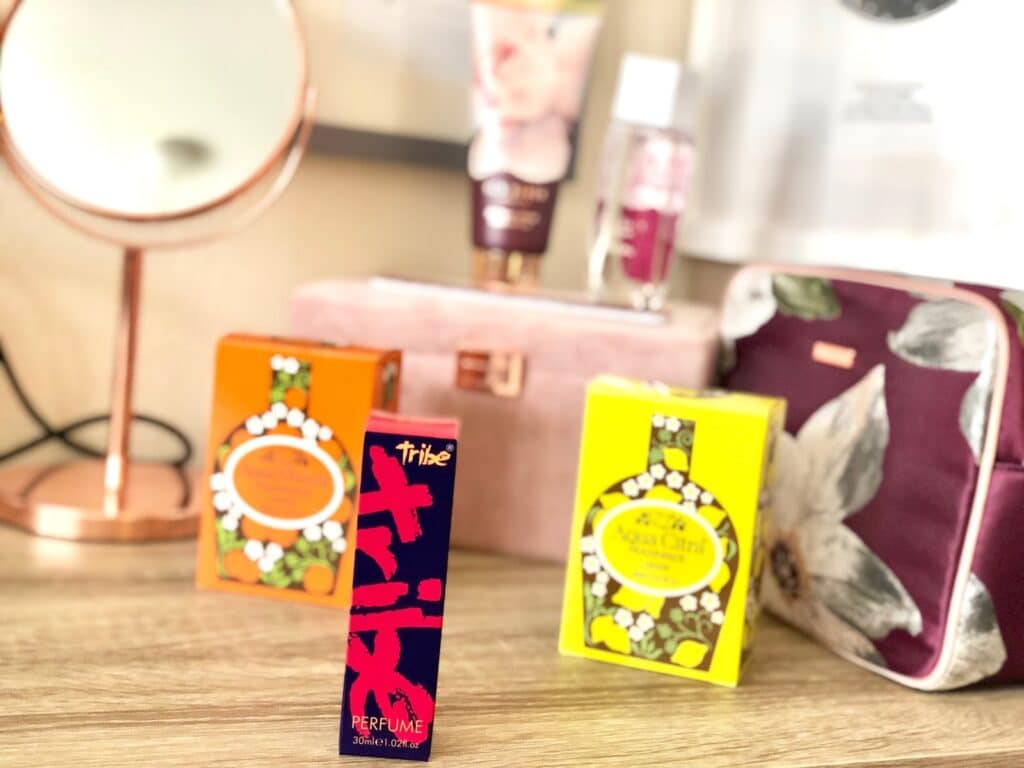 A collection of beauty products, including lotion and a make-up bag, is displayed on a wooden surface with vintage fragrances and retro perfumes showcased beside a mirror and decorative items in the background.