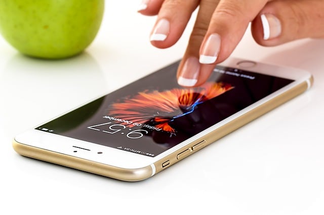 A person with a French manicure is using a gold mobile lying on a white surface, with a green apple in the background. The phone displays the time and a colourful lock screen, hinting at how to unlock your handset for free.
