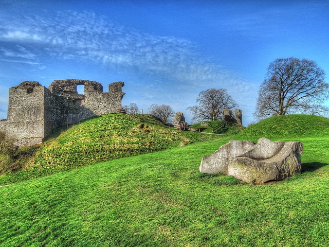 Ruins of an old stone castle on a grassy hill, perfect for family walks, with scattered trees in the background and a large weathered rock formation in the foreground under a blue sky with wispy clouds.