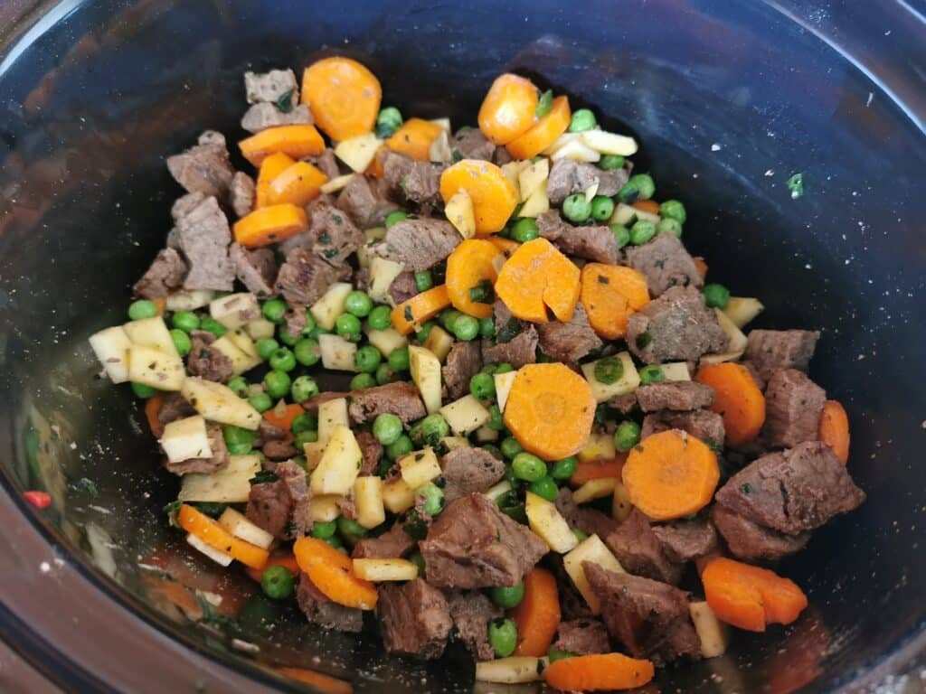 A close-up of a slow cooker filled with chopped beef, sliced carrots, green peas, and diced potatoes—one of those family favourite meal ideas everyone will love.