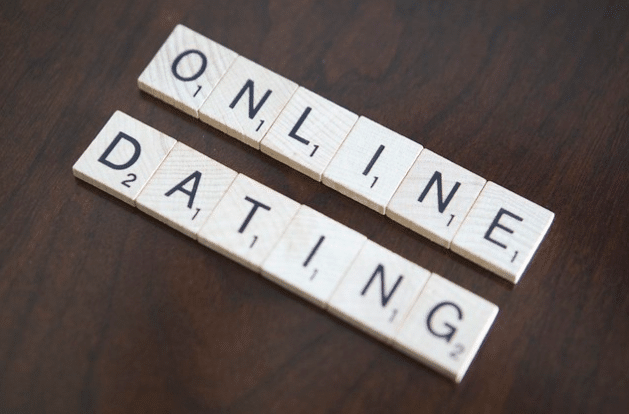 Scrabble tiles on a wooden surface spell out "ONLINE DATING" in two rows, reminding everyone to keep dating safety in mind whilst meeting new people.