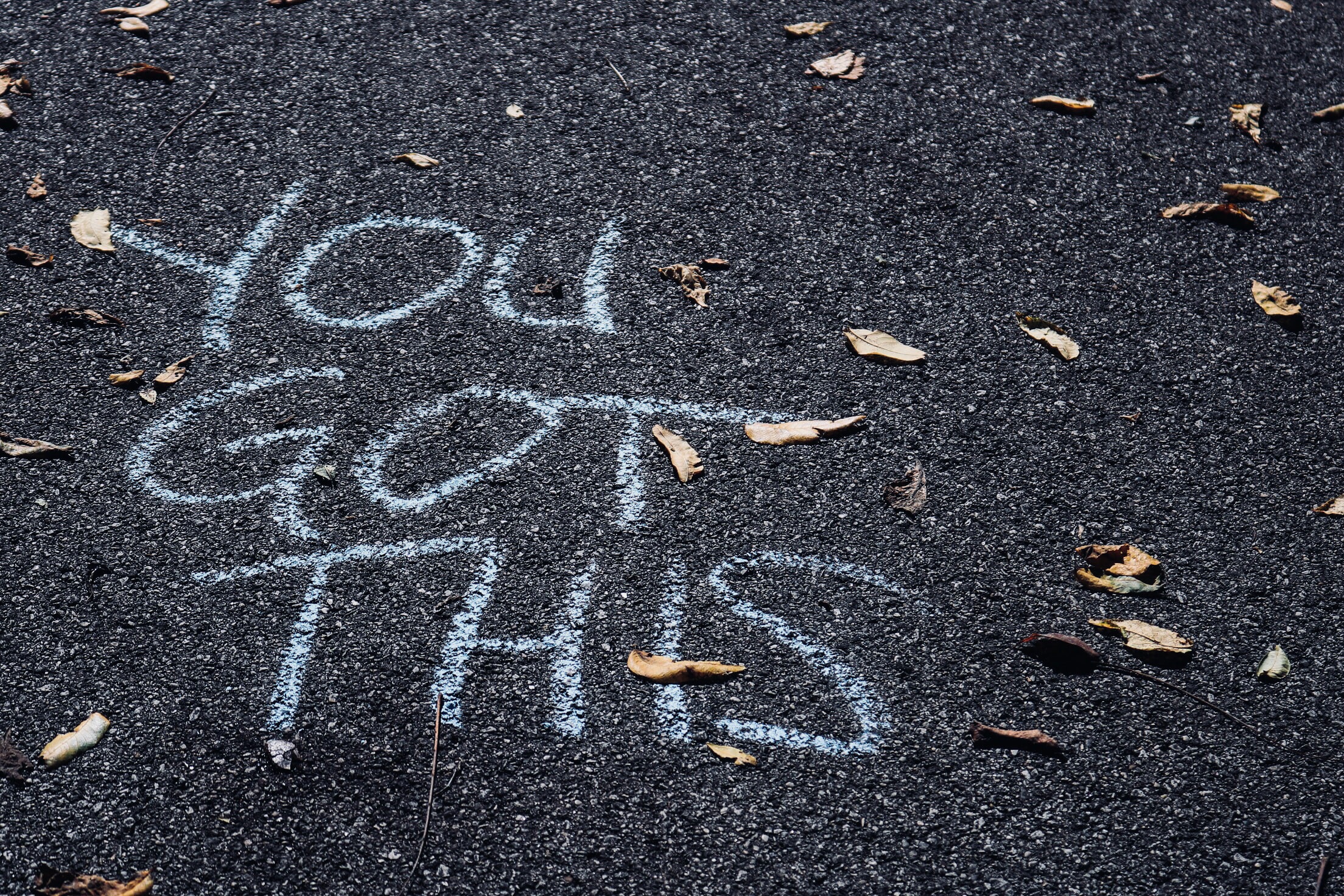 White chalk message "YOU GOT THIS" is written on a dark tarmac surface, surrounded by scattered dried leaves—a simple reminder and one of those self-esteem boosting tips you might find on a walk.