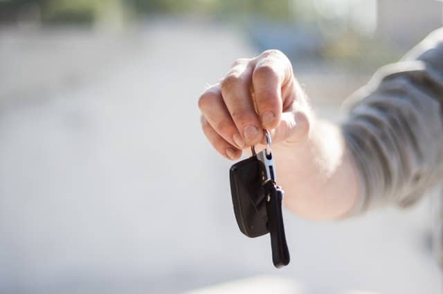 A close-up of a person’s hand holding out a car key and remote, with a blurred background. The focus is on the hand and key, suggesting handing over or receiving car keys—highlighting insurance benefits such as Black Box Insurance.