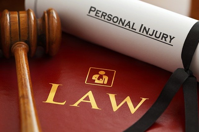 A wooden judge’s gavel rests beside a rolled document labelled "Personal Injury," atop a red book marked "LAW"—symbolising the personal injury sector and its crucial role in legal matters.