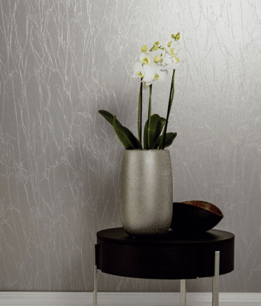 A silver vase with white orchids and green leaves sits on a round dark wooden table next to a decorative object, bringing modern colour ideas to life against a light grey textured wall in this modern master bedroom.