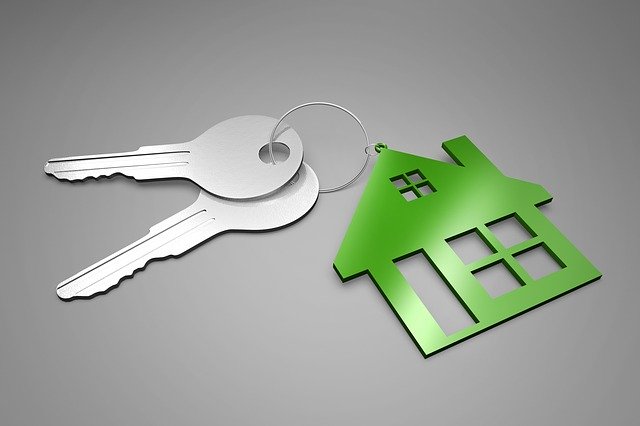 Two silver keys on a keyring with a green house-shaped keyring, placed on a grey surface—perfect for showcasing landlord qualities or symbolising the search for a good landlord.