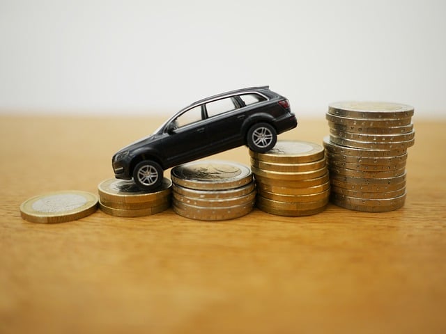 A small toy car is positioned on top of several stacks of coins arranged in ascending order, symbolising Car Finance on a wooden surface with a plain background.