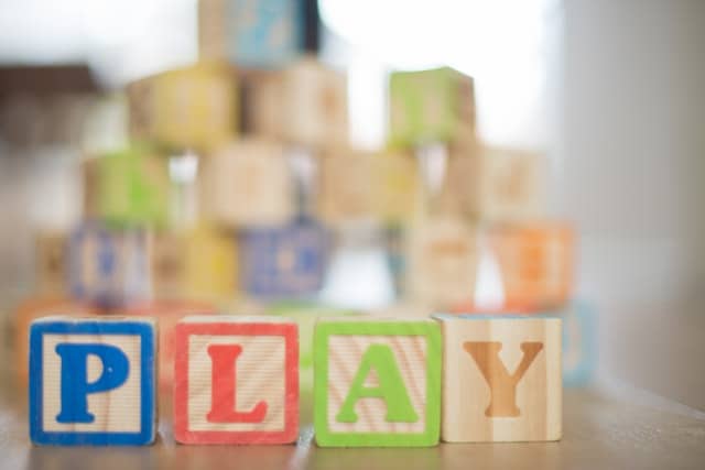 Colourful wooden blocks spelling "PLAY" are arranged in the foreground, with more stacked blocks blurred behind—a bright, cheerful scene that evokes the playful atmosphere of finding childcare that’s just right for your little one.