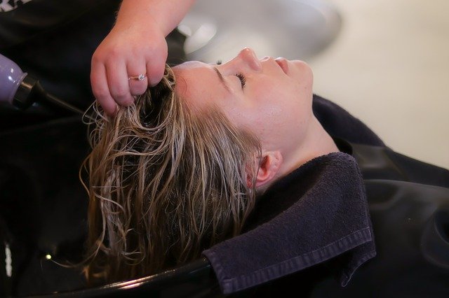 A person with wet hair reclines at a salon basin while another massages their scalp, offering gentle hair protection. A dark towel supports the neck, highlighting the importance of summer hair care during every wash.
