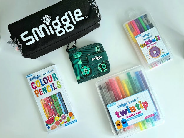 A flat lay of my favourite things from Smiggle stationery, including a black pencil case, a green wallet, scented coloured pencils, a scented twin tip marker pack, and a doughnut-themed gel pen set.
