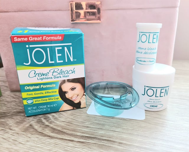 A box of Jolen Creme Bleach is shown next to its contents—one of my favourite things: a small blue mixing cup, a white jar labelled "Jolen Creme," a tube labelled "accelerator," and a spatula, all placed on a wooden surface.