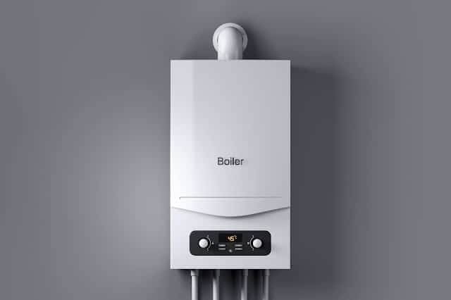 A modern white wall-mounted boiler with a digital display and control buttons, connected to several pipes, installed on a grey wall—a great example of equipment that benefits from regular boiler servicing.