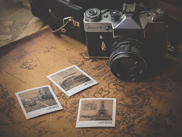 A vintage Zenit-E camera rests on an old map next to three instant photos featuring landmarks, perfect inspiration for family travel and exploring child-friendly destinations. A black camera case strap is also visible in the background.