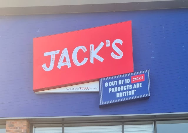 A shopfront sign reads "JACK'S" in bold white letters on a red background. A smaller sign next to it says "8 OUT OF 10 JACK'S PRODUCTS ARE BRITISH," highlighting the shop's commitment to budget-friendly shopping.