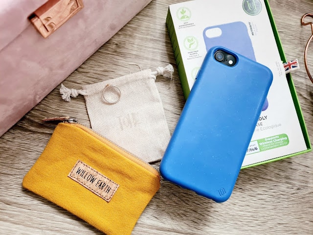A blue phone case rests on its packaging beside a small cream drawstring pouch with a ring on top and a yellow zip pouch labelled "Willow Earth," all from Wearth London, perfect for anyone passionate about ethical shopping.