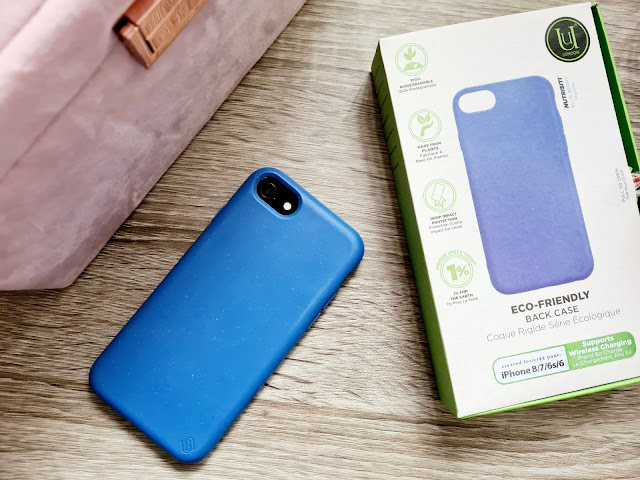 A blue phone case on an iPhone next to its green and white eco-friendly packaging, highlighting features like wireless charging support, 1% for the Planet, and ethical shopping with Wearth London. A pink bag is partially visible in the background.