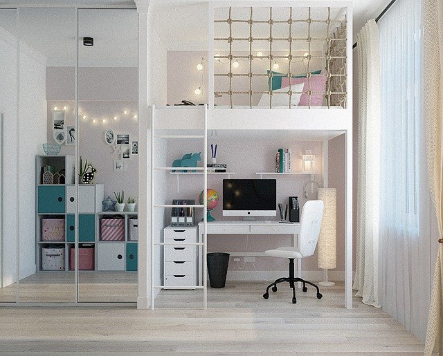 A modern kids' room makeover featuring a loft bed above a white desk and computer, quirky kids' room decor like colourful storage boxes, bookshelves, fairy lights, and a large window with sheer curtains.