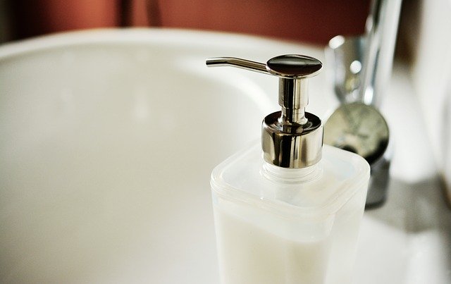 A close-up of a soap dispenser with a pump, placed on the edge of a white bathroom basin with a chrome tap in the background—an inspiring touch for your Bathroom Design.