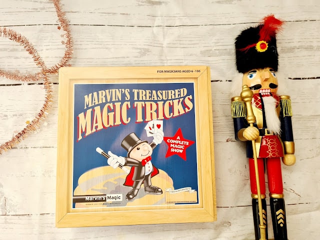 A wooden box labelled “Marvin’s Treasured Magic Tricks” sits on a light surface next to a traditional nutcracker figure—a charming scene perfect for children and featured in this year’s Christmas Gift Guide.