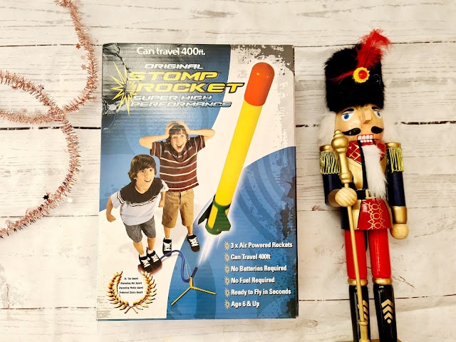 Box of the "Original Stomp Rocket" featuring two excited children and a large rocket illustration, next to a festive wooden nutcracker figure on a white wooden background—an ideal pick for Christmas Gifts for Children.
